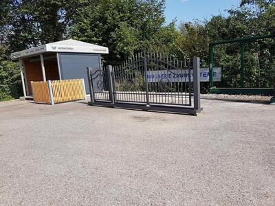 Ausstellung von einem Eisen-Gitter-Tor und ein hellbraunen Zaun neben einem offenem Häuschen