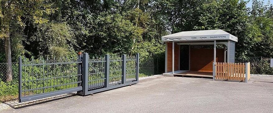 Ein kleiner Metallzaun mit einem Holzlattenzaun im Hintergrund