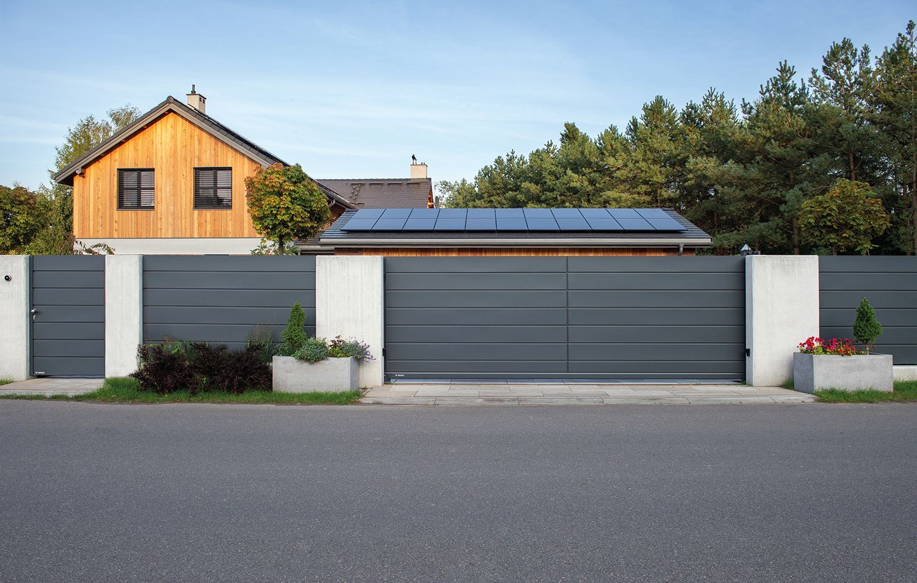Grauer Zaun mit passendem Hoftor, dahinter ist ein Haus mit einem Solarpanel auf dem Dach installiert
