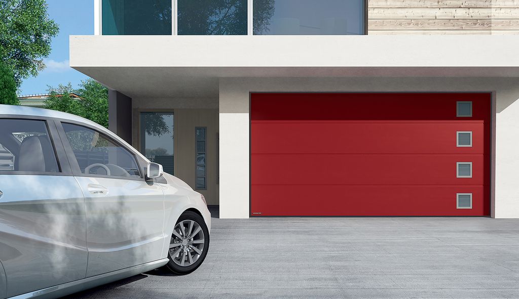 Ein modernes Haus mit rotem Garagentor vor dem ein graues Auto steht