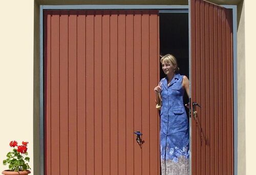 Eine Frau öffnet ein braunes Flügeltor